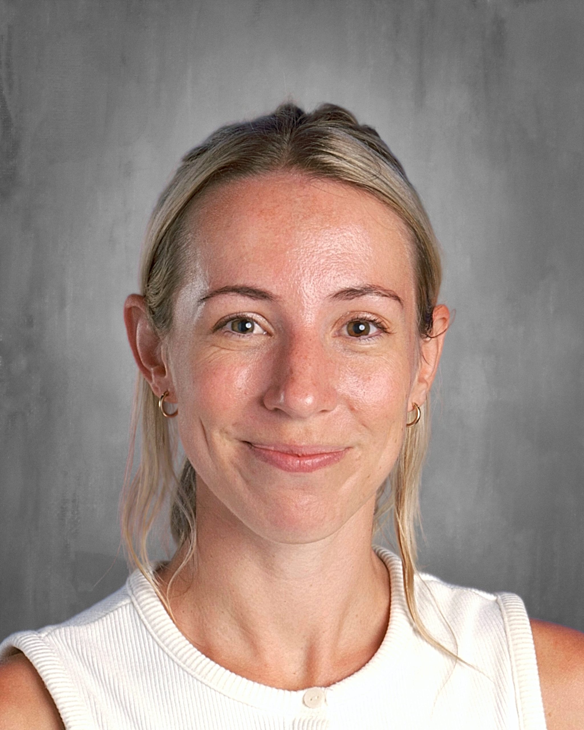 Smiling woman with light hair in a white top against a gray background.
