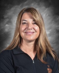 A woman with long, brown hair smiles confidently, wearing a black jacket with "MUSD" printed on it, against a gray background.