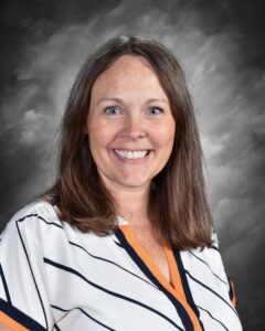 Smiling woman with long brown hair wearing a striped shirt, set against a gray background.