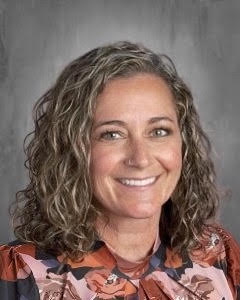 Smiling woman with curly hair wearing a floral blouse, posed against a gray background.
