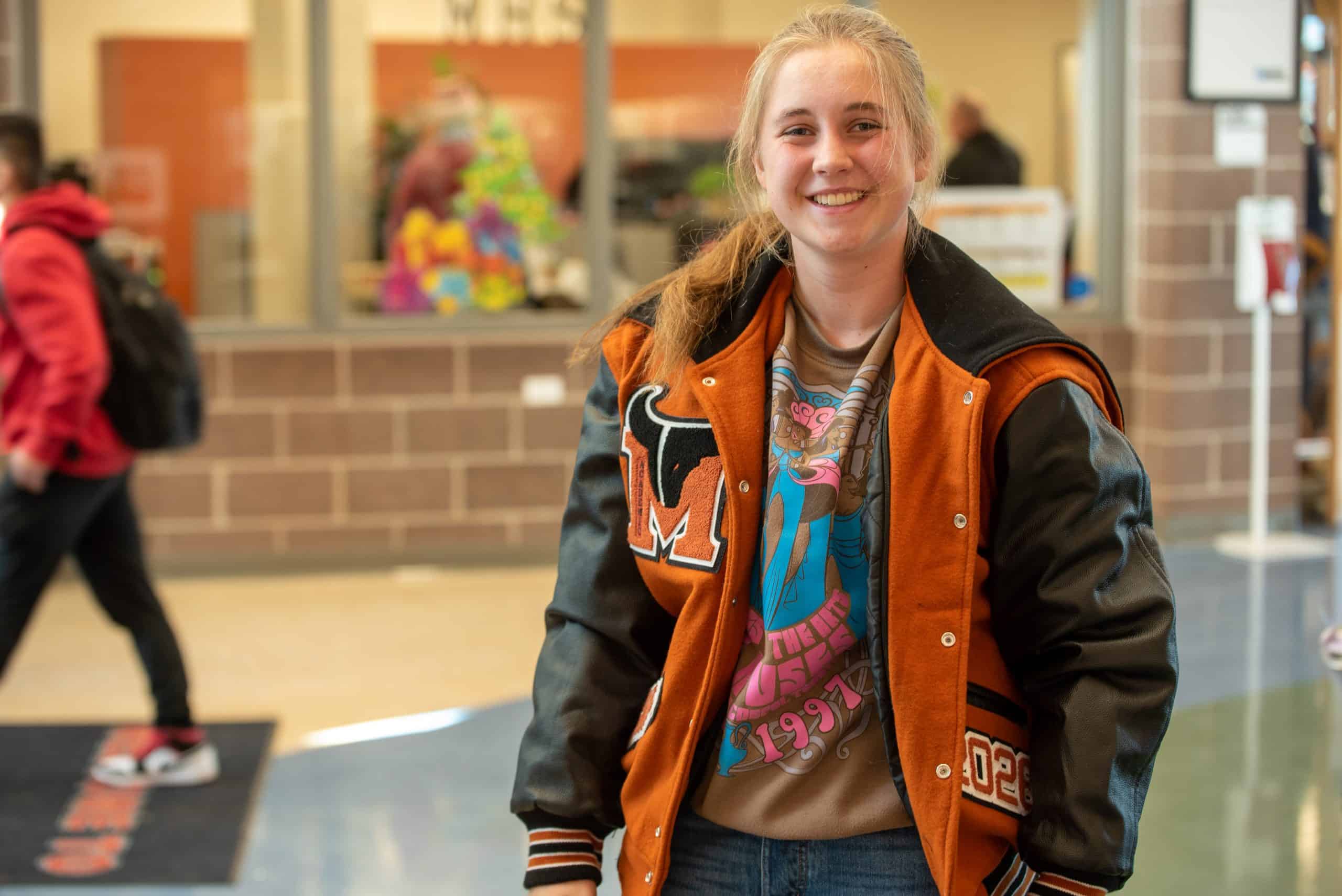 Female high school student trying on her new letterman jacket on in the school lobby.