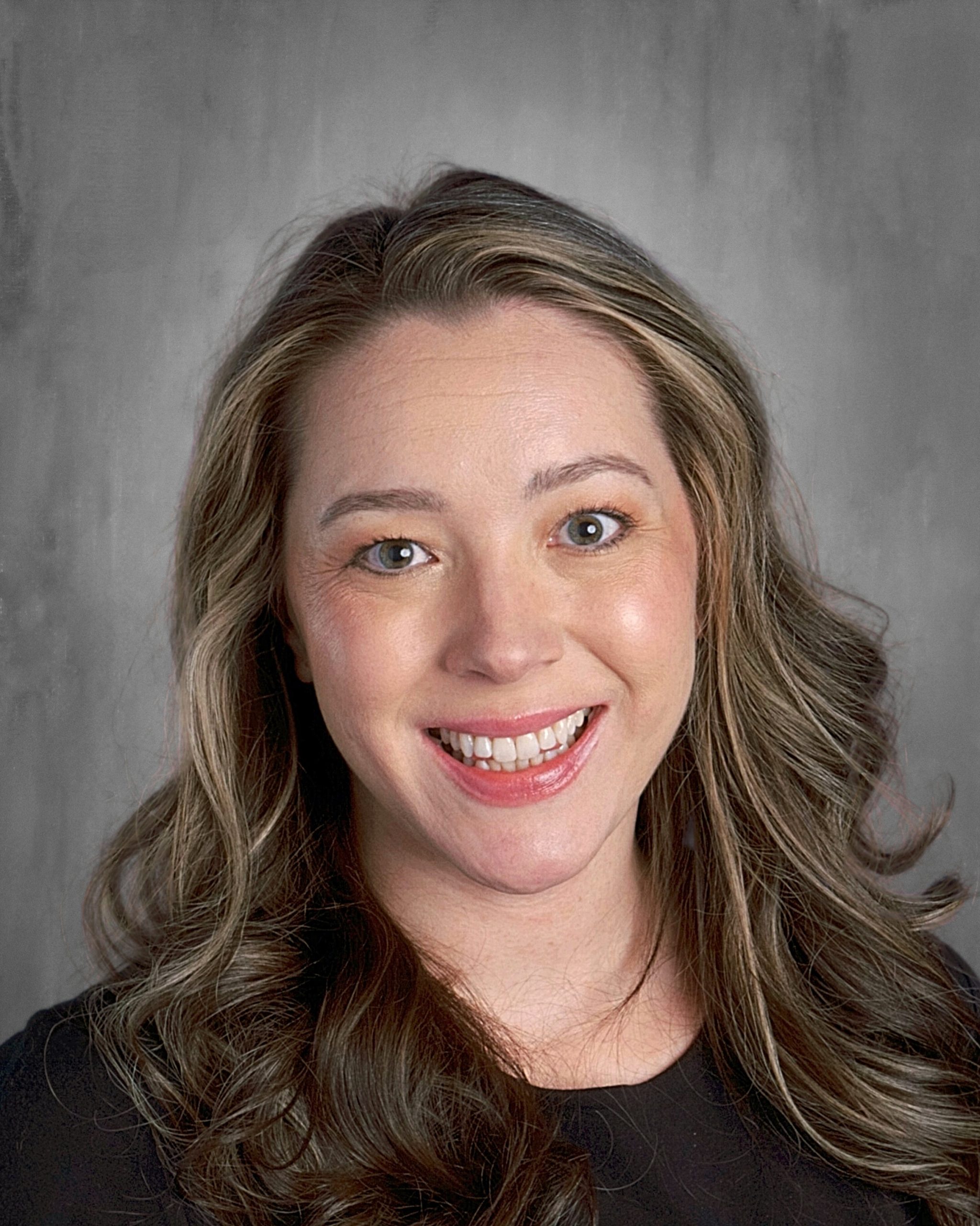 Smiling person with wavy brown hair against a gray background.
