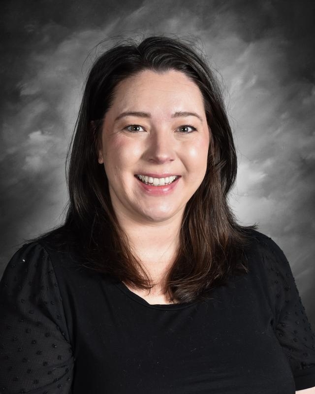 Smiling woman with long dark hair, wearing a black top, against a gray background.